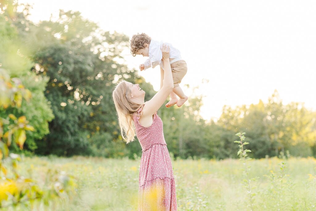 Mom holds son over her head during family photo session with Sara Sniderman Photography at Green Way in Wayland Massachusetts
