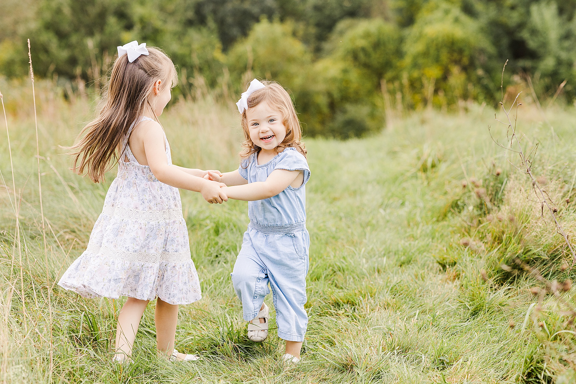 sisters hold hands during family photo session with Sara Sniderman Photography at Oak Grove Park in Millis Massachusetts