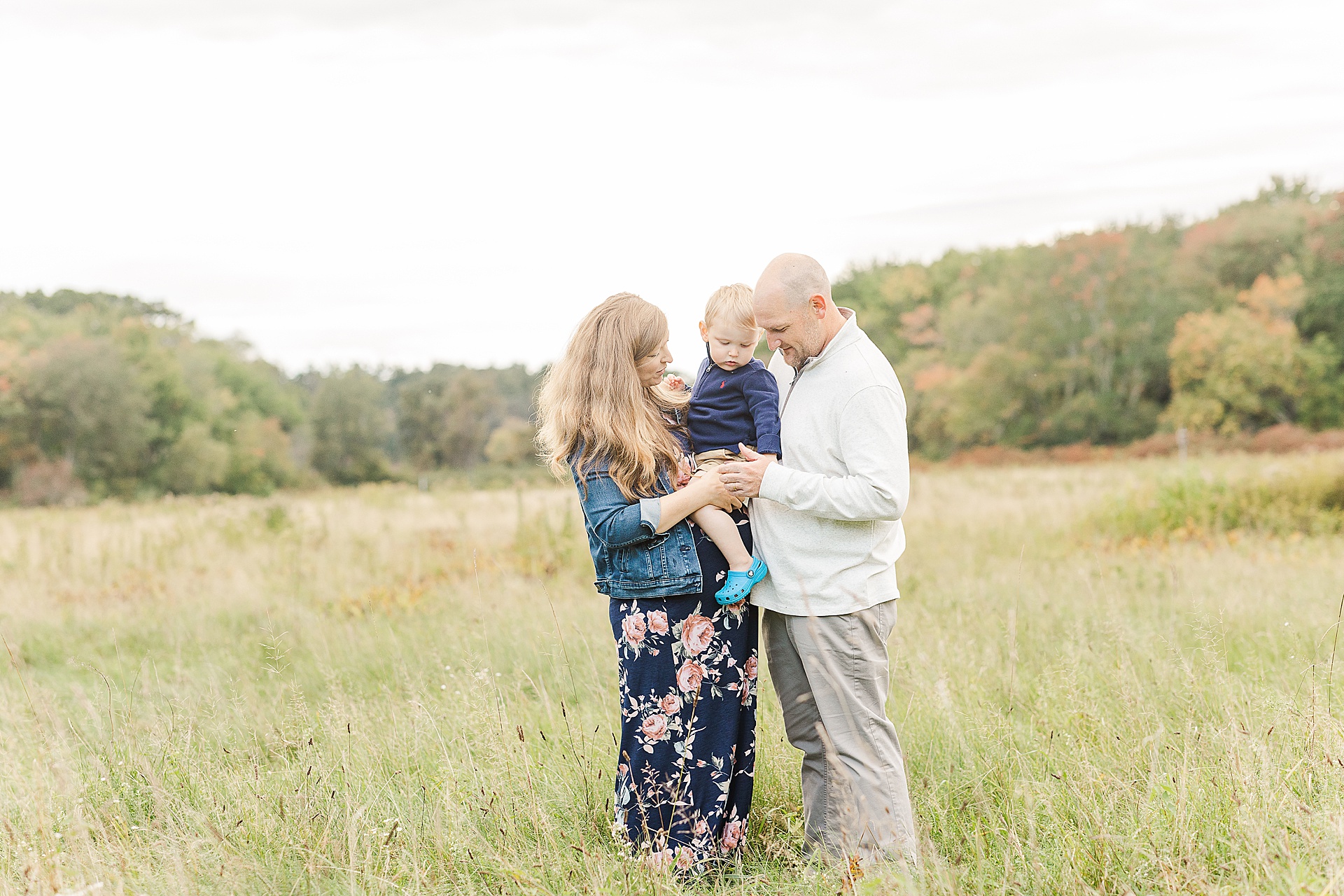 parents hold toddler during maternity photo session with Sara Sniderman Photography at Cow Common in Wayland Massachusetts