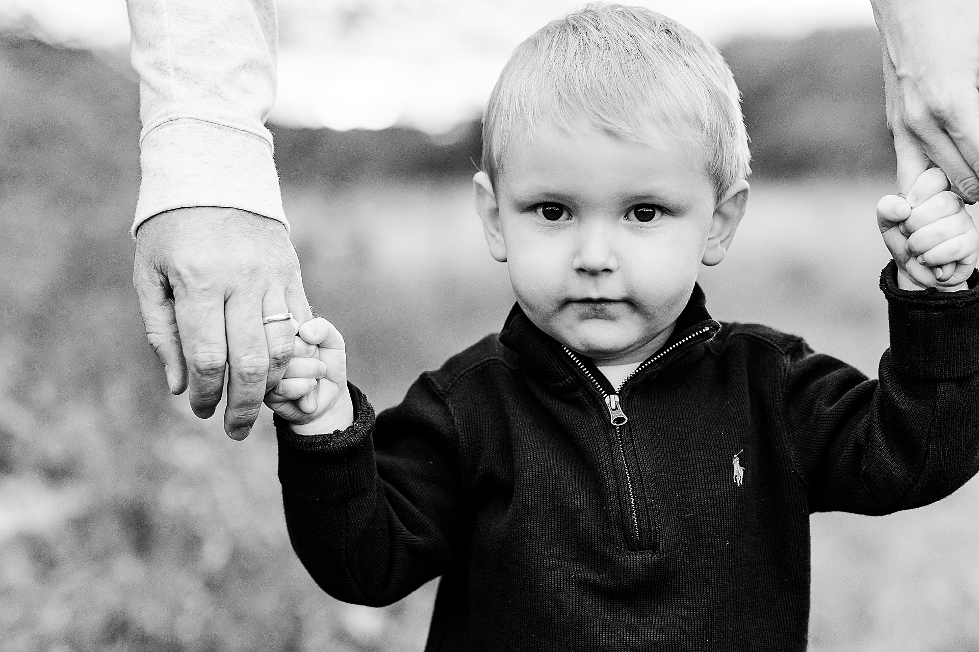 black and white of toddler holding parents hands during maternity photo session with Sara Sniderman Photography at Cow Common in Wayland Massachusetts