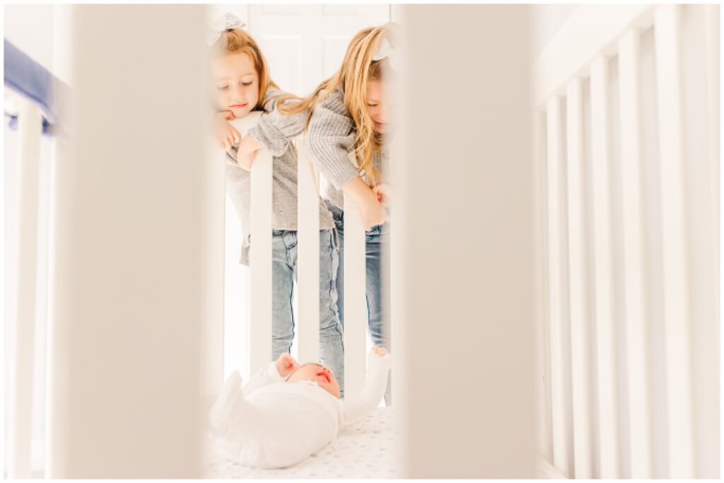 sisters looking into crib at newborn brother during in home newborn photo session with Sara Sniderman Photography in Sherborn Massachusetts