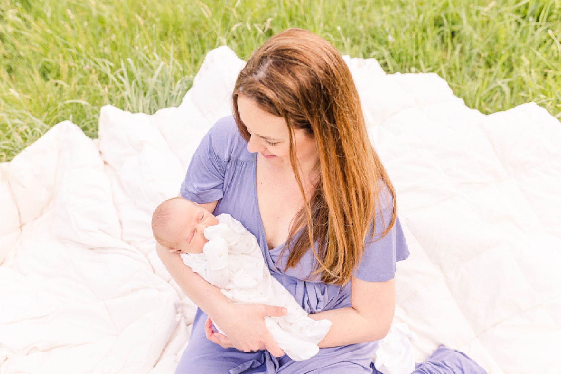 mom sits on blanket in a field holding baby during outdoor newborn photo session with Sara Sniderman Photography at Heard Farm Wayland Massachusetts