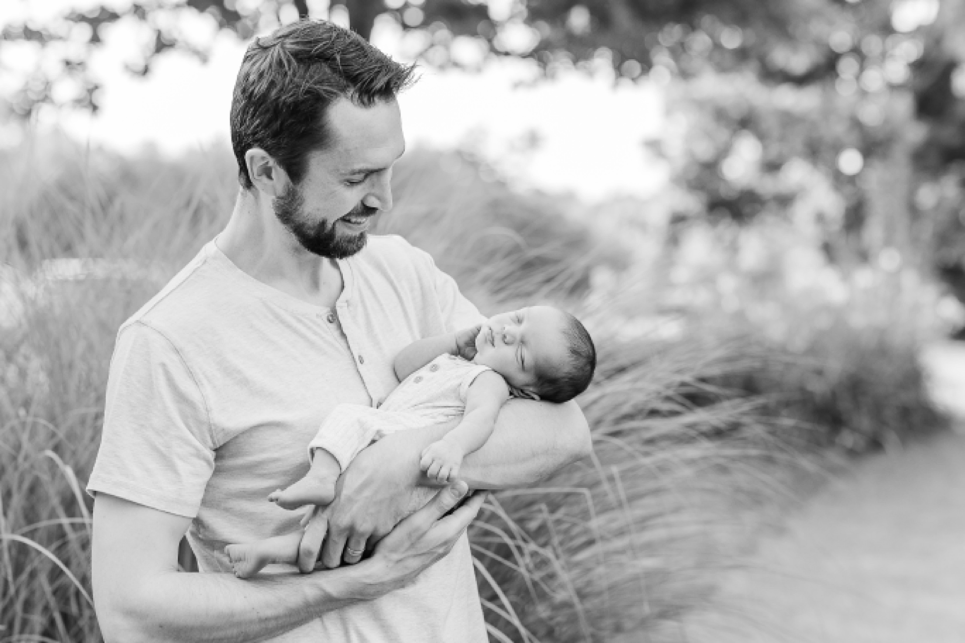 black and white of father holding baby during outdoor newborn photo session with Sara Sniderman Photography at Oak Grove Park Millis Massachusetts