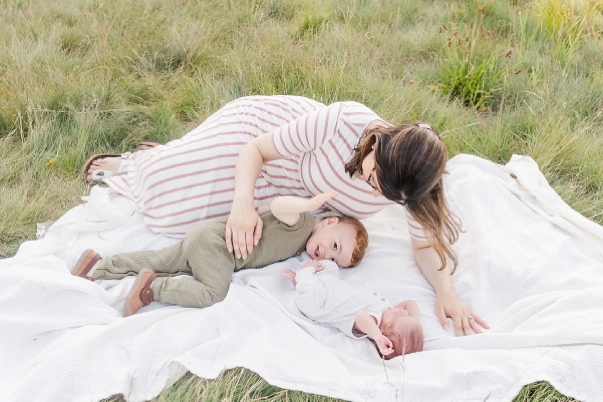 mom lays on blanket with toddler and baby during outdoor newborn photo session with Sara Sniderman Photography at Oak Grove Park Millis Massachusetts