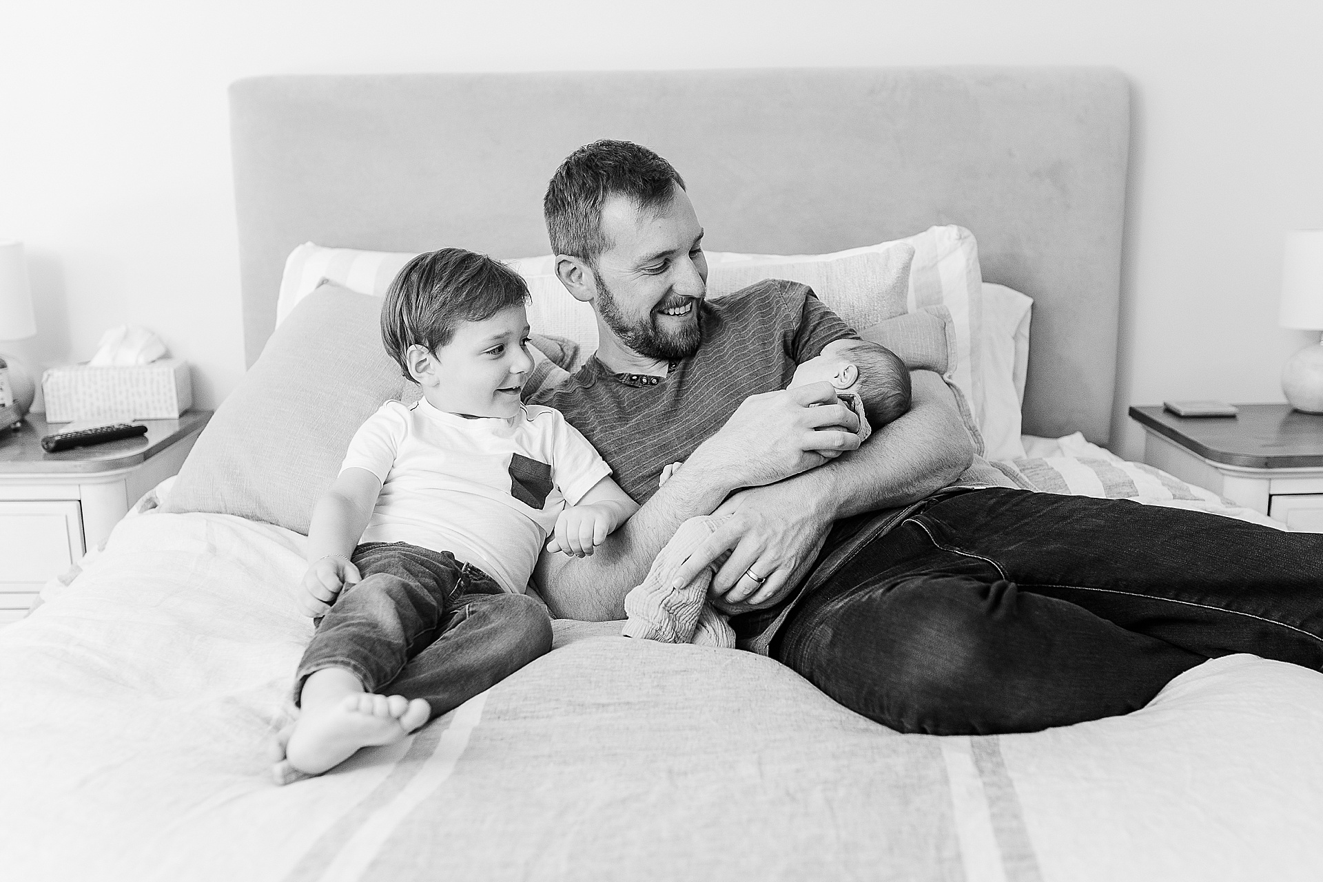 black and white of father with two sons on bed during in home newborn photo session with Sara Sniderman Photography Southborough Massachusetts