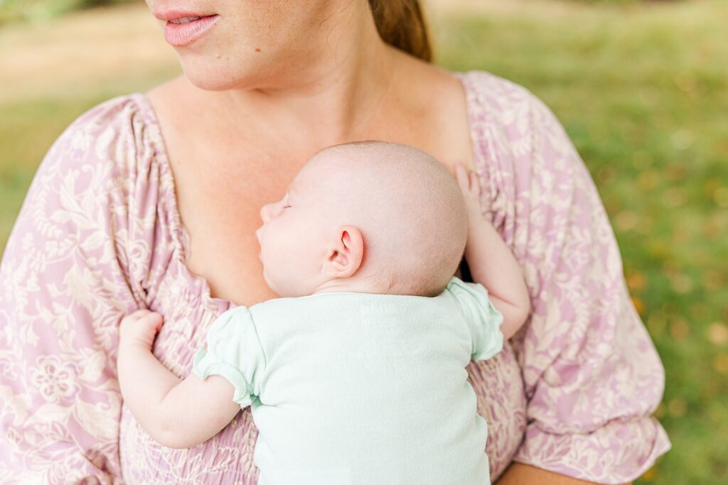 Mother holds baby on chest during outdoor newborn photo session with Sara Sniderman Photography in Natick Massachusetts