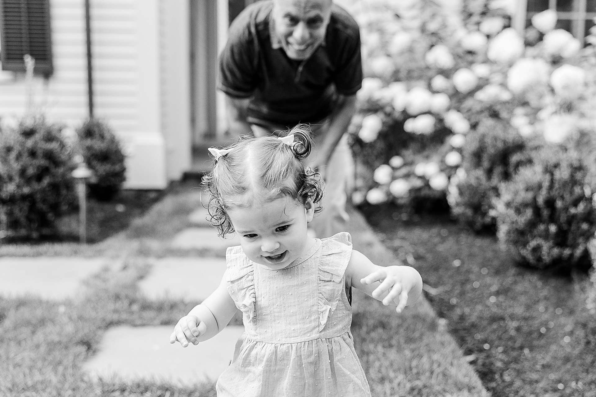 black and white of toddler running and grandfather smiling at her during family photo session with Sara Sniderman Photography in Newton Massachusetts