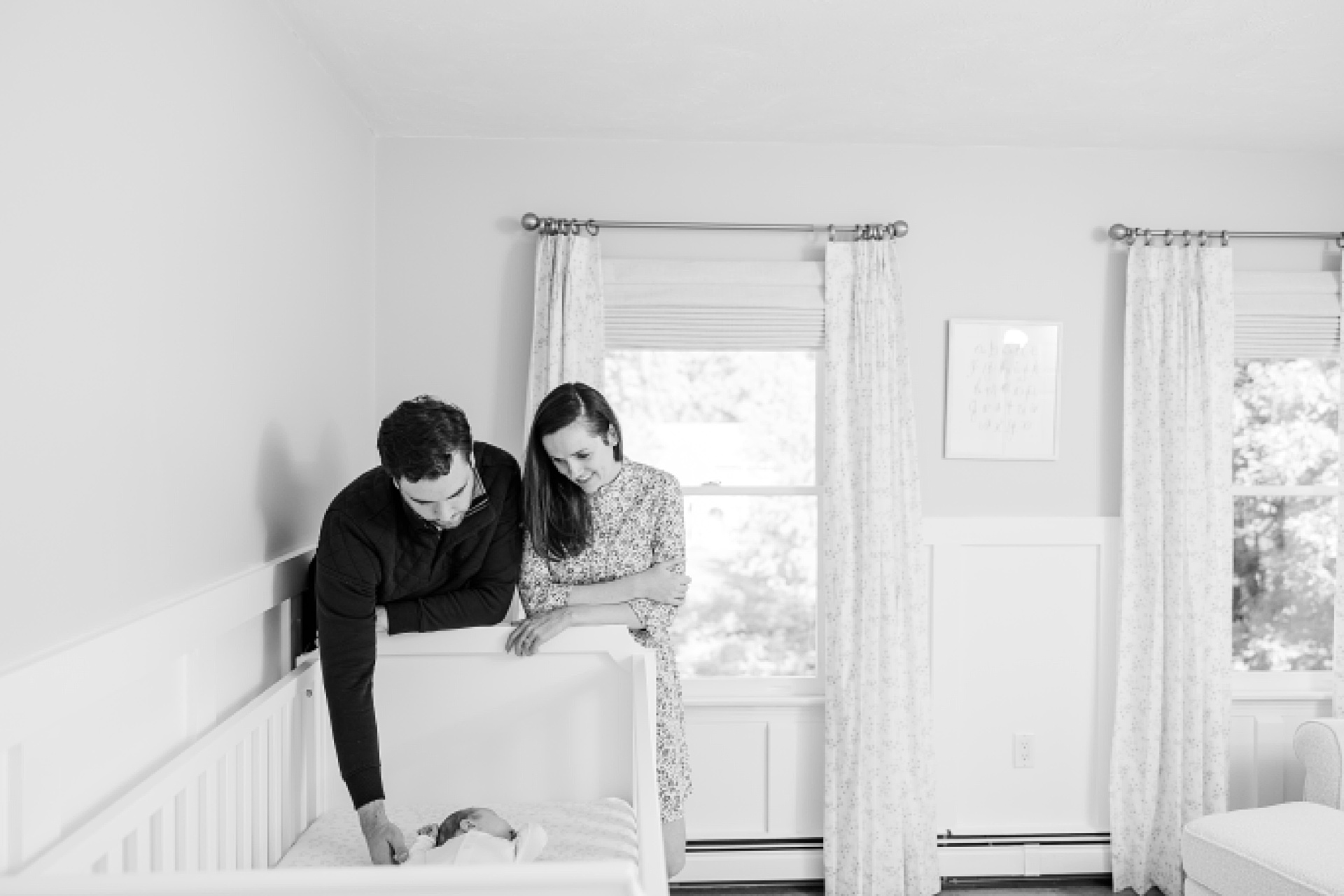 black and white of parents looking to baby crib during in home newborn photo session with Sara Sniderman Photography in Natick Massachusetts