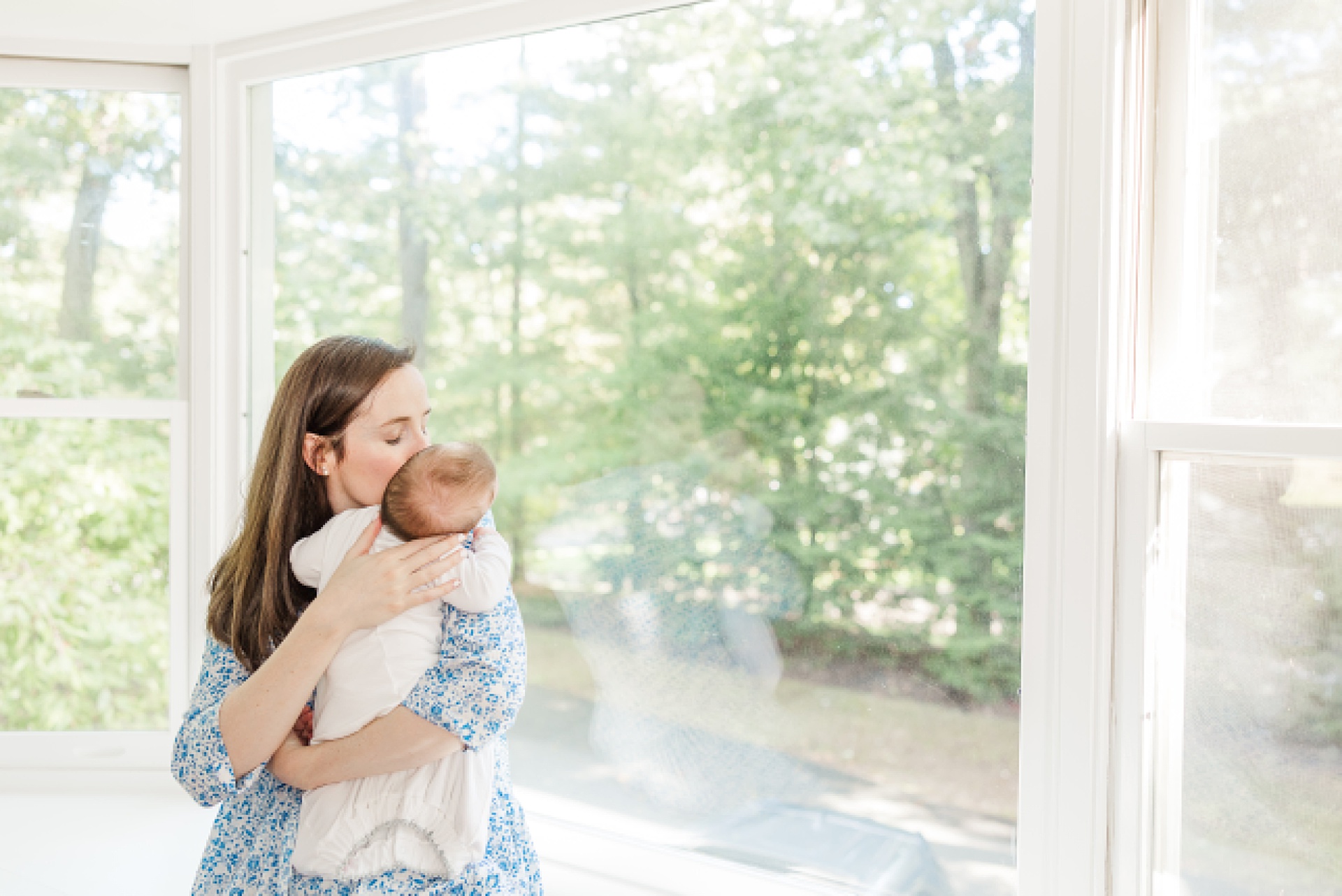 mom holds baby by window during in home newborn photo session with Sara Sniderman Photography in Natick Massachusetts