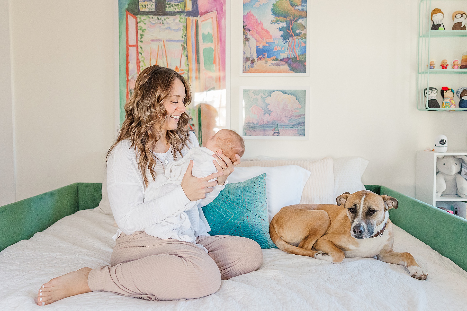 mom sits on bed with baby and dog during in home newborn photo session for NICU baby in Natick Massachusetts