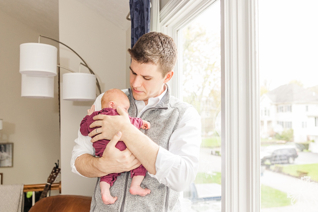dad holds baby by window during Lifestyle newborn photo session in Needham Massachusetts with Sara Sniderman Photography