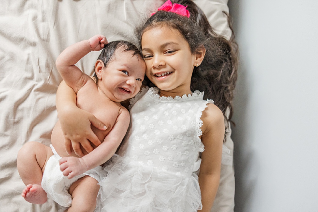 sister lays on bed with baby in home newborn photography in Natick Massachusetts with Sara Sniderman Photography