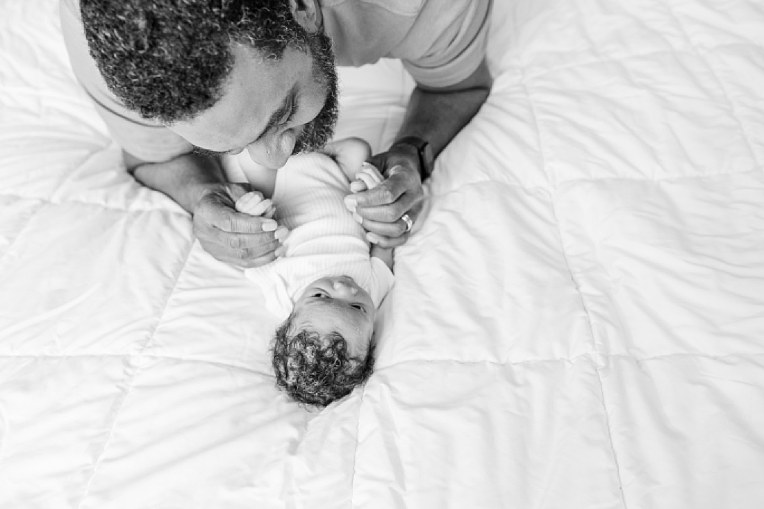 black and white of dad on bed with baby during lifestyle newborn photo session in metro west Boston with Sara Sniderman Photography
