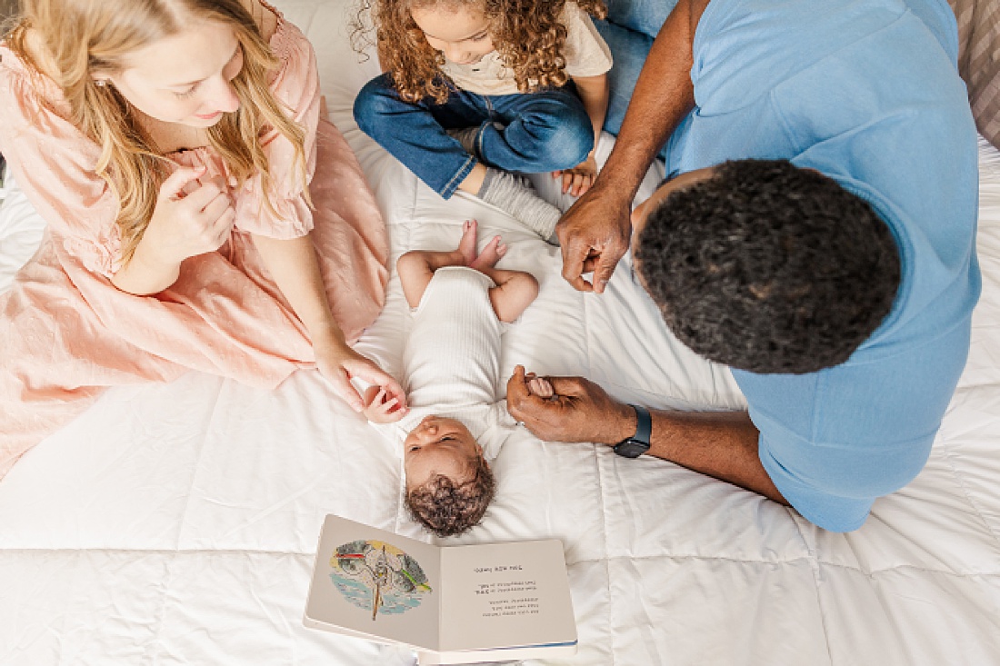 family reads baby a book during lifestyle newborn photo session in metro west Boston with Sara Sniderman Photography
