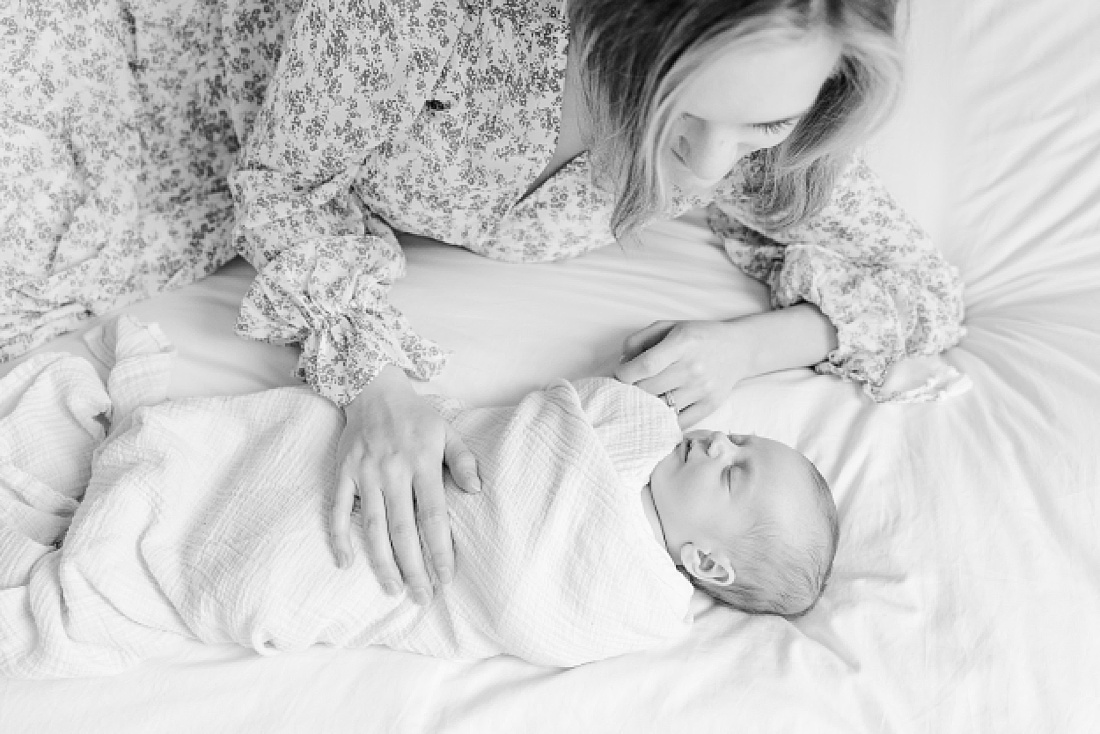 black and white photo of mom on bed with baby during in home newborn photo session in Natick Massachusetts with Sara Sniderman Photography