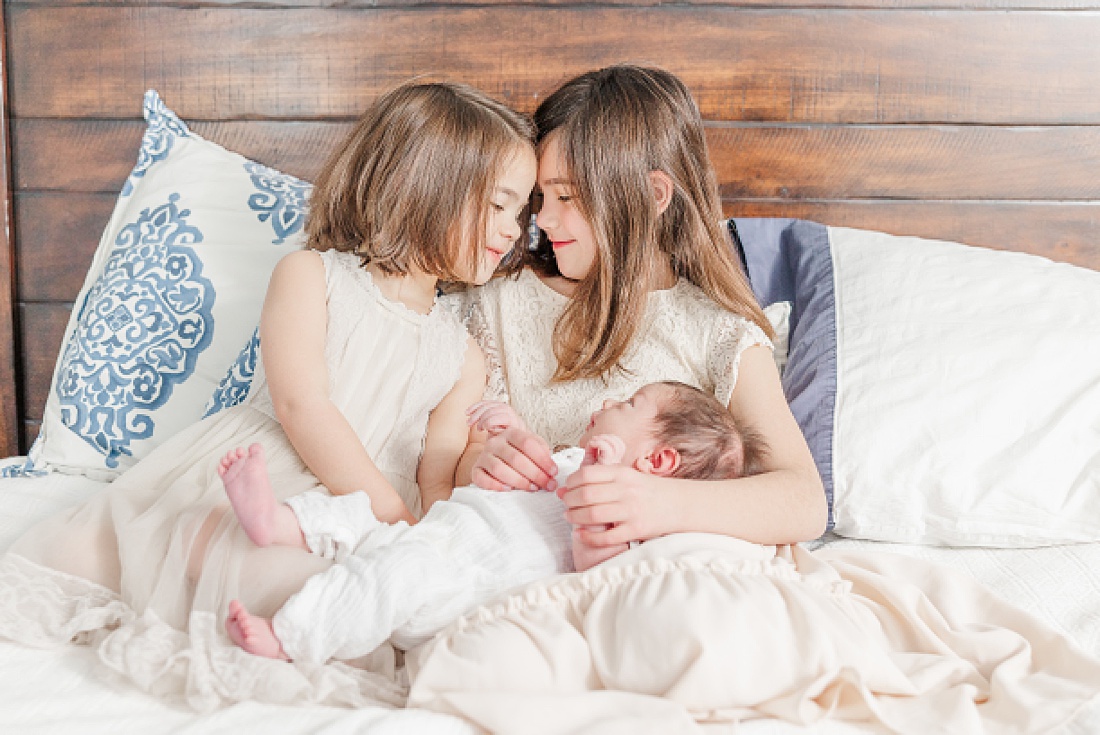 sisters hold baby during in-home newborn photo session with Sara Sniderman Photography in Needham Massachusetts