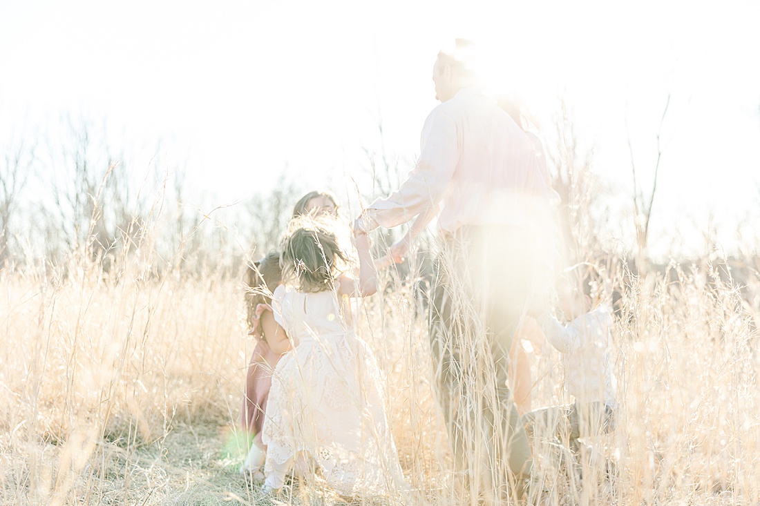 family plays ring around the rosey during winter photo session in tall golden grass at medfield state hospital with Sara Sniderman Photography
