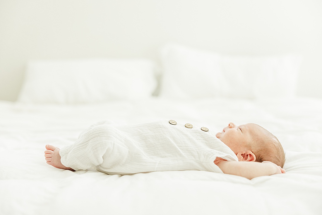 baby lays on a bed during in-home photo session in Millis Massachusetts with Sara Sniderman Photography