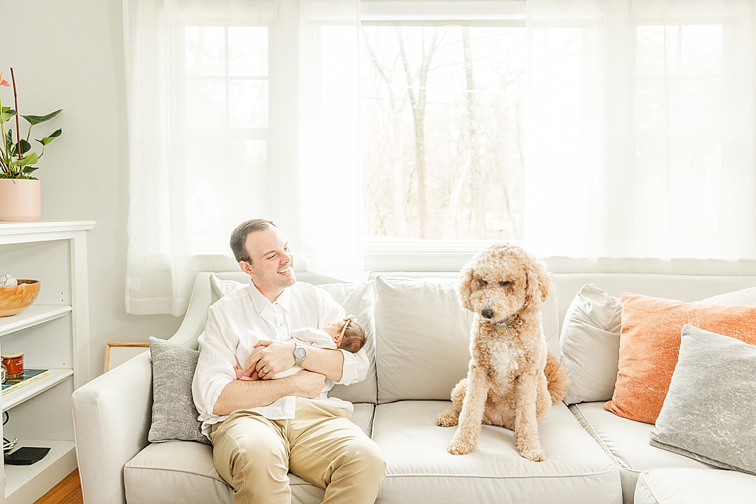 man on couch with baby and dog during in home family photo session with Sara Sniderman Photography in Metro West Boston