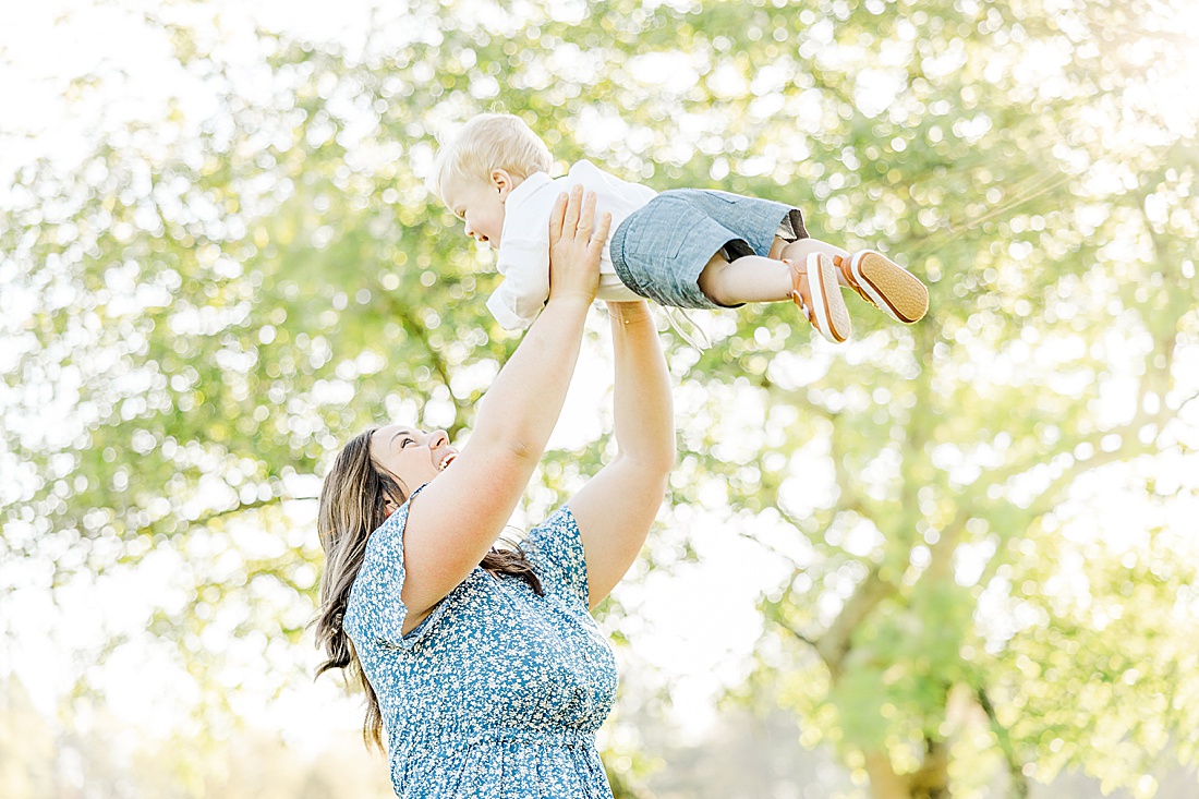 mother holds son up high during Spring Morning family photo session at Sprindale field in Dover Massachusetts with Sara Sniderman Photography.