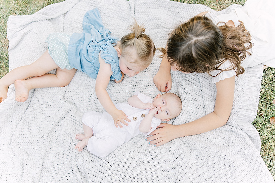 Image of professional family photo session taken by Sara Sniderman Photography, a family, newborn and maternity photographer serving the Metro West Boston area include: Natick, Needham, Newton, Wellesley, Wayland, Weston, Sherborn, Sudbury, Southborough, Medfield, Medway, Holliston, Framingham. The image is of sisters on blanket with newborn baby sister. 