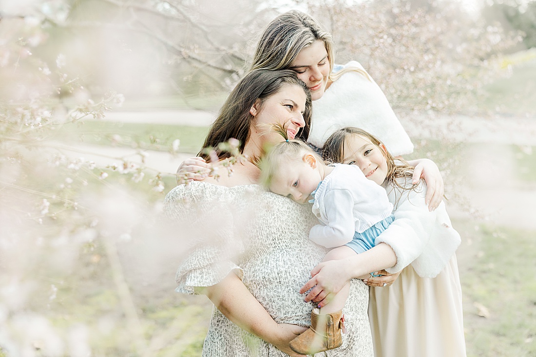 Image of professional family photo session taken by Sara Sniderman Photography, a family, newborn and maternity photographer serving the Metro West Boston area include: Natick, Needham, Newton, Wellesley, Wayland, Weston, Sherborn, Sudbury, Southborough, Medfield, Medway, Holliston, Framingham. The image is of girls hugging their pregnant mom. 