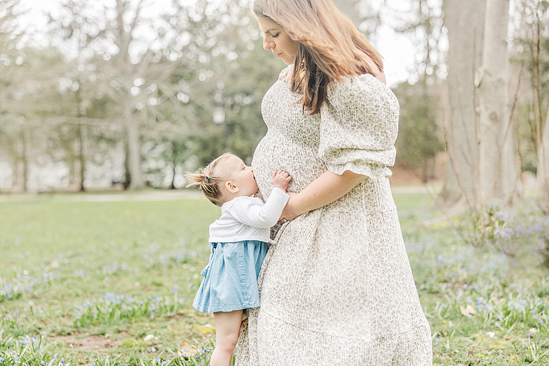 Image of professional family photo session taken by Sara Sniderman Photography, a family, newborn and maternity photographer serving the Metro West Boston area include: Natick, Needham, Newton, Wellesley, Wayland, Weston, Sherborn, Sudbury, Southborough, Medfield, Medway, Holliston, Framingham. The image is of girl kissing mothers belly.