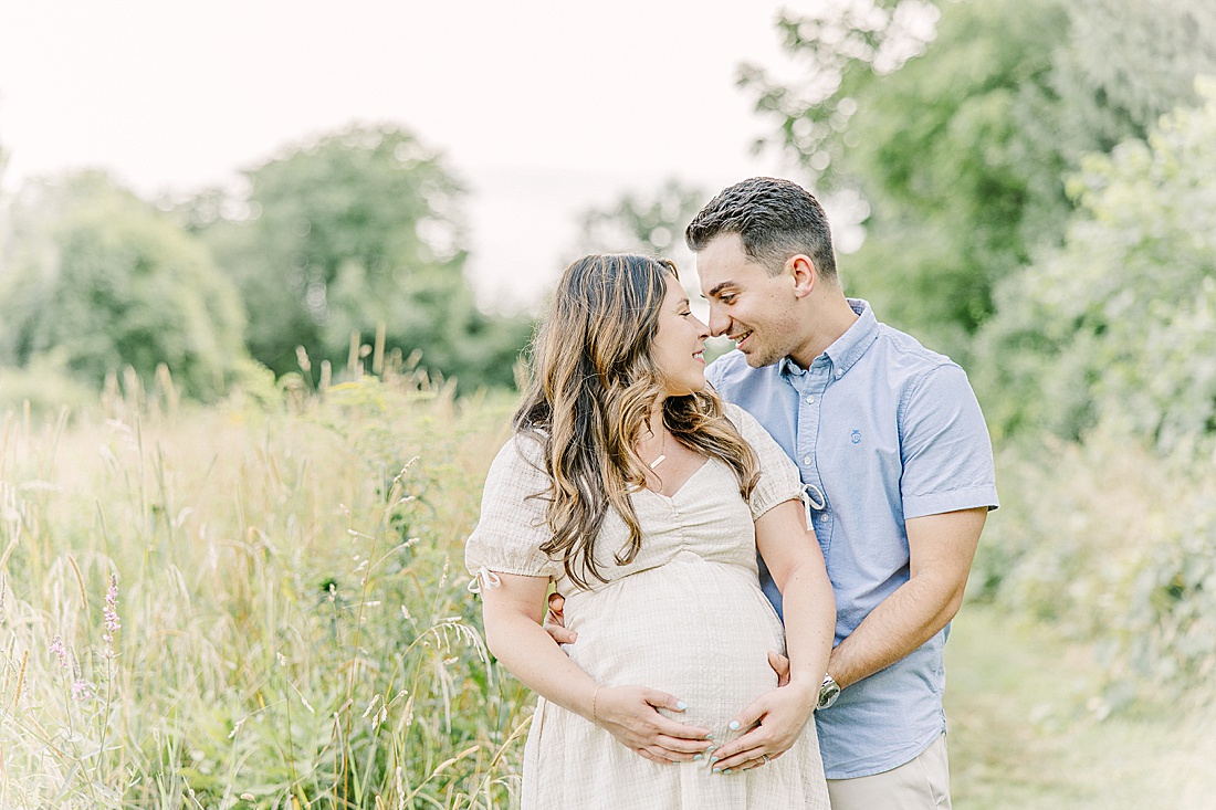 Image of professional maternity photos taken by Sara Sniderman Photography, a family, newborn and maternity photographer serving the Metro West Boston area include: Natick, Needham, Newton, Wellesley, Wayland, Weston, Sherborn, Sudbury, Southborough, Medfield, Medway, Holliston, Framingham. Image shows couple nose to nose while holding pregnant belly.