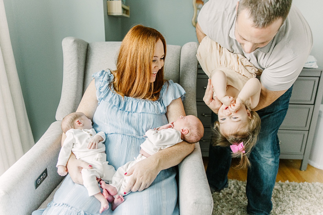 mom holds babies while dad holds toddler upside down during twin newborn photo session in Natick Massachusetts with Sara Sniderman Photography