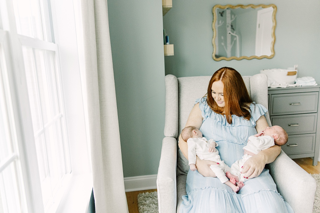 mom sits in chair holding babies during twin newborn photo session in Natick Massachusetts with Sara Sniderman Photography