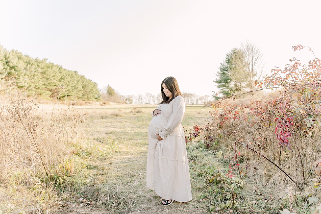 mother holds belly in field during maternity photo session with Sara Sniderman Photography in Needham Massachusetts