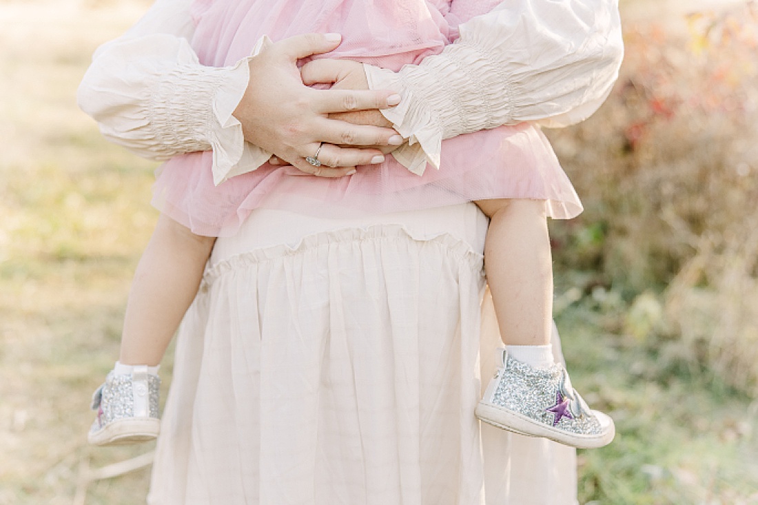 mother holds daughter on belly during maternity photo session with Sara Sniderman Photography in Needham Massachusetts