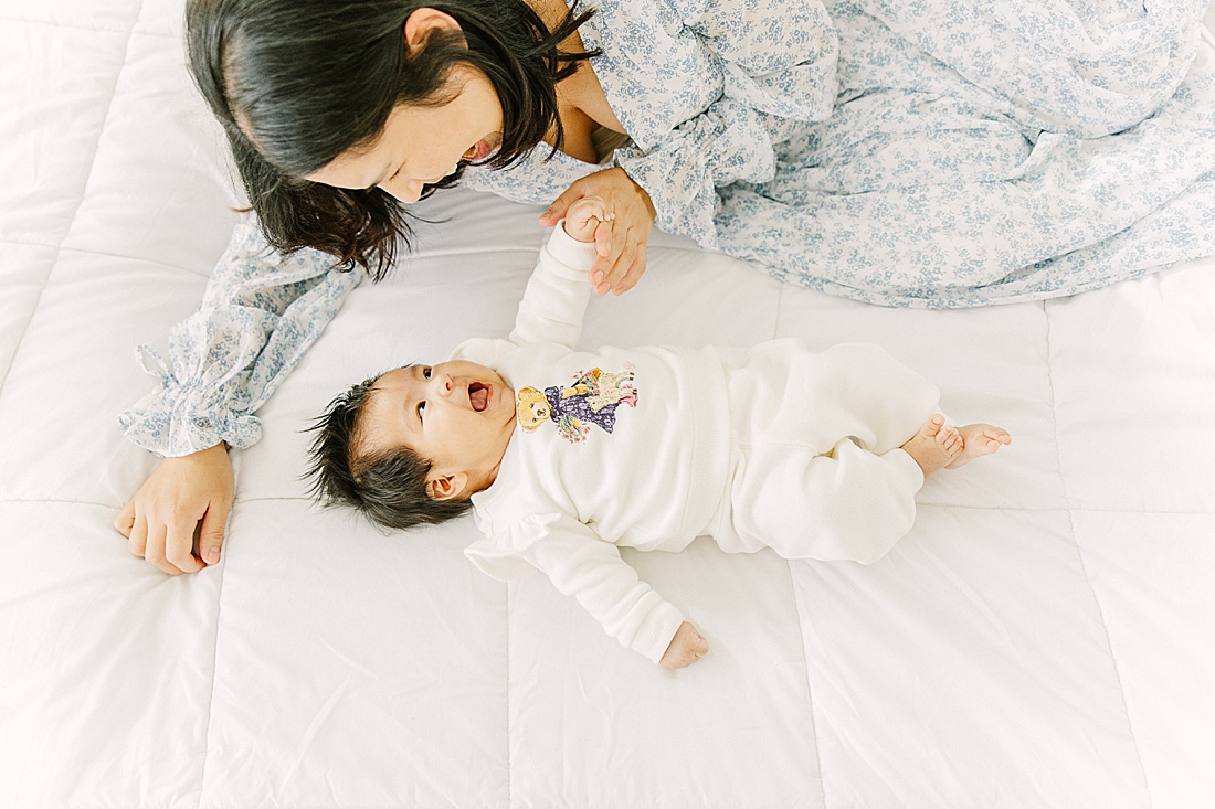 mom lays on bed with baby during studio lifestyle photo session with Sara Sniderman Photography in Natick Massachusetts