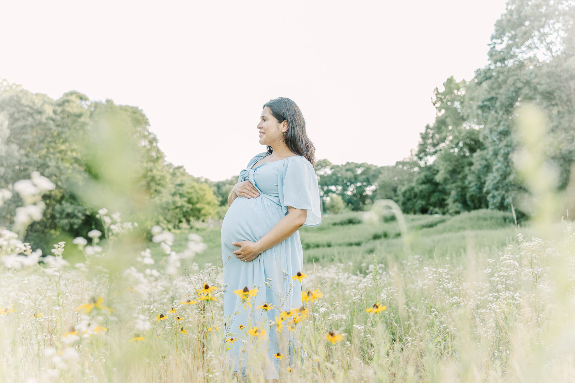 pregnant woman stands in wild flower field during maternity photo session with Sara Sniderman Photography in Newton Massachusetts