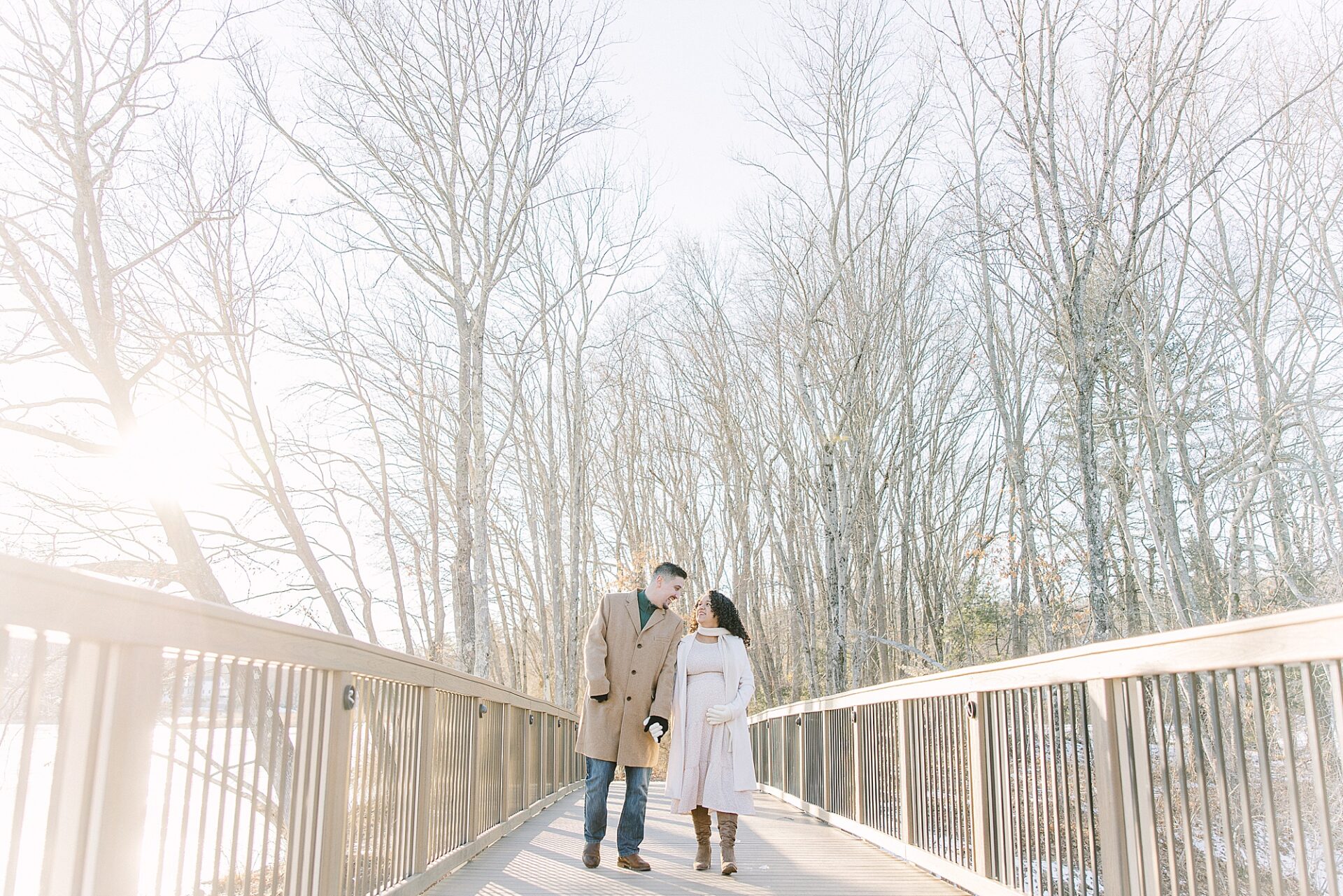 couple walks across bridge during snowy winter maternity session at Ashland Reservoir with Sara Sniderman Photography.