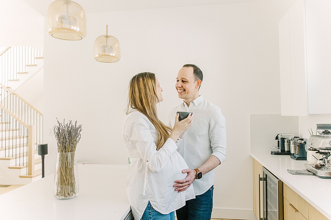 couple stands in kitchen with wife holding a cup of coffee during an in-home maternity photo session with Sara Sniderman Photography in Newton Massachusetts