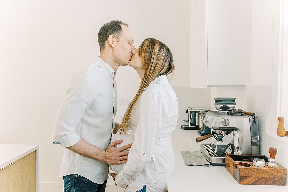 couple kiss in kitchen during an in-home maternity photo session with Sara Sniderman Photography in Newton Massachusetts