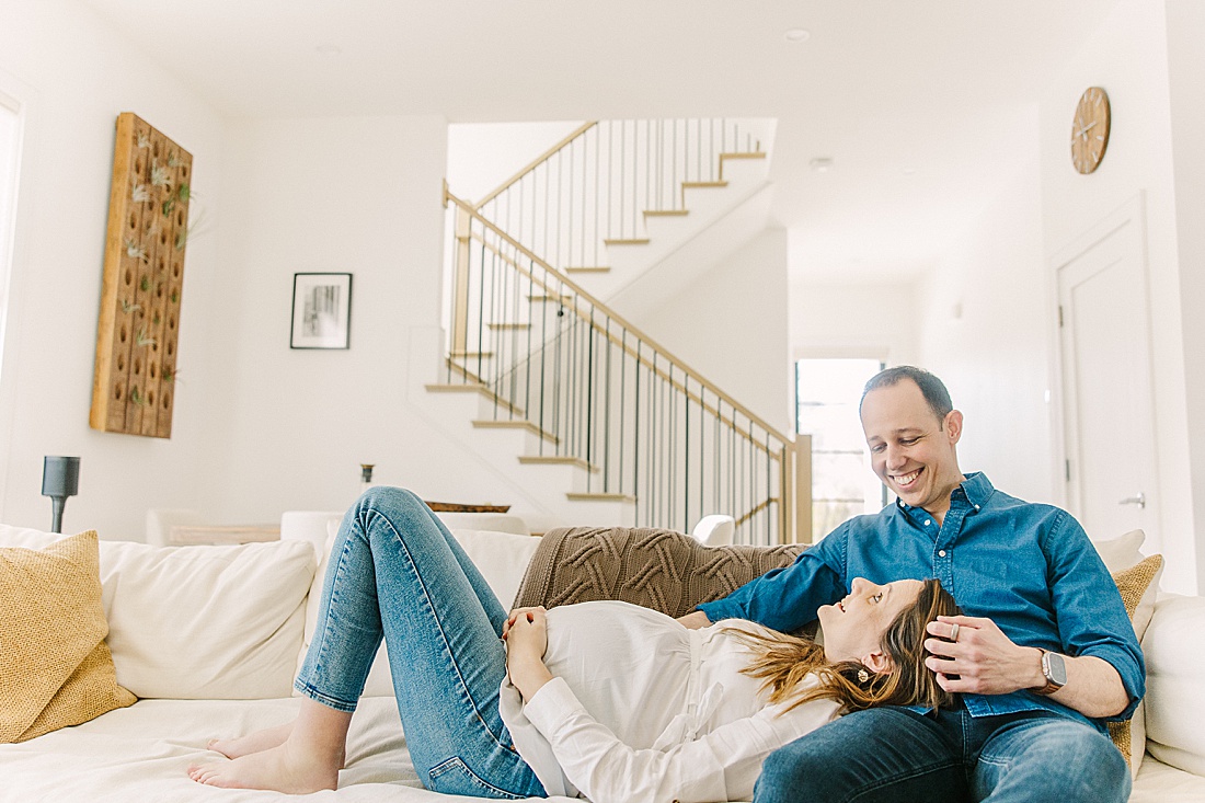 woman lays on husbands lap during an in-home maternity photo session with Sara Sniderman Photography in Newton Massachusetts