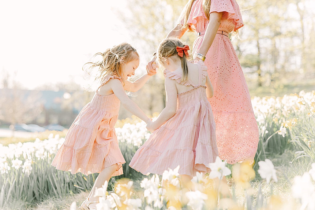 mother and twin girls play ring around the rosey in daffodils field during family photo session with Sara Sniderman Photography at Wellesley College. 