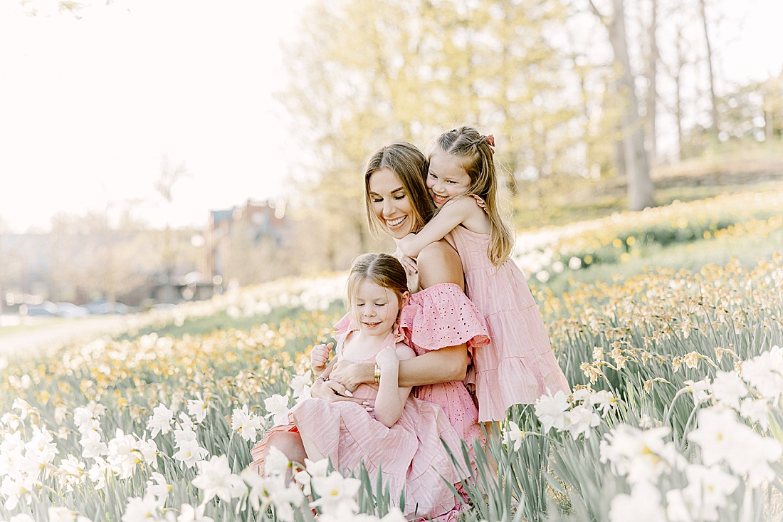 Mother and twin daughters sit in field of daffodils during family photo session with Sara Sniderman Photography at Wellesley College.