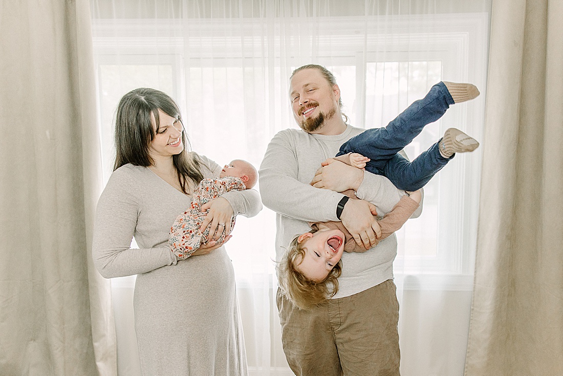 mom holds baby and dad holds toddler upside down during newborn photo session with Sara Sniderman Photography in Natick Massachusetts