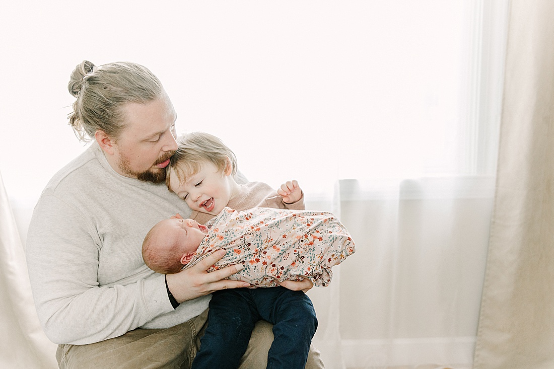 father holds toddler and baby during newborn photo session with Sara Sniderman Photography in Natick Massachusetts