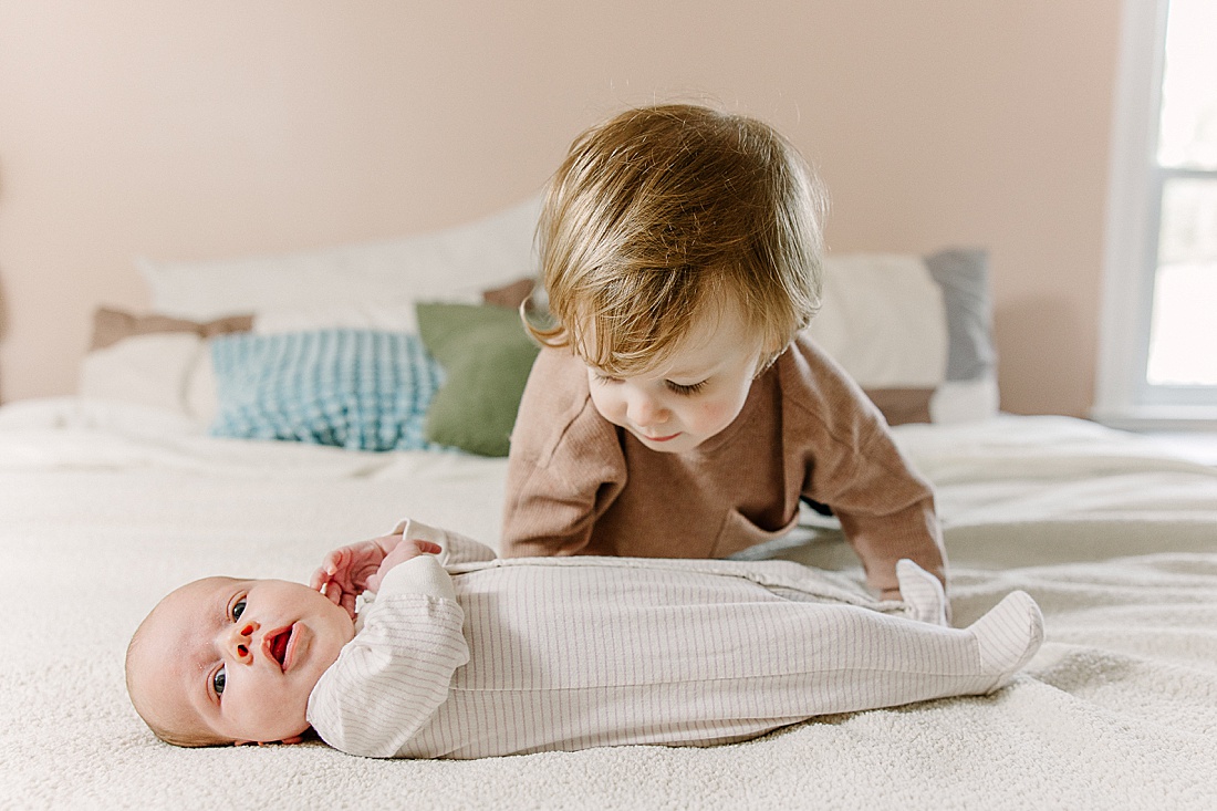 toddler looks at baby on bed during newborn photo session with Sara Sniderman Photography in Natick Massachusetts