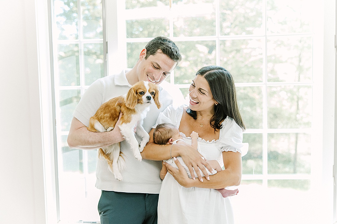 dad holds dog and mom holds baby during in-home newborn photo session with Sara Sniderman Photography in Natick Massachusetts