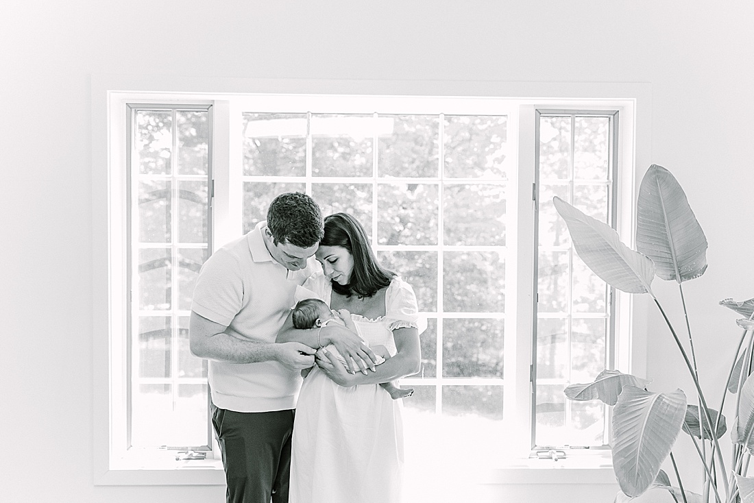 black and white of parents holding baby by window during in-home newborn photo session with Sara Sniderman Photography in Natick Massachusetts