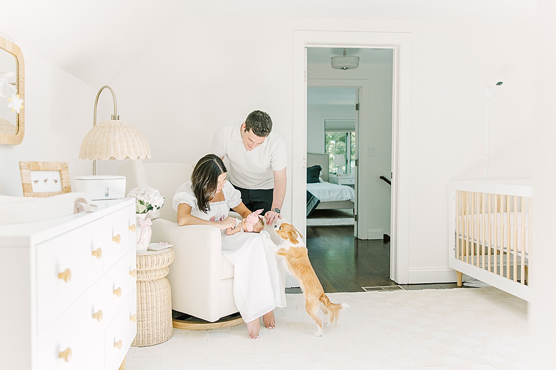 mother sits in rocking chair with baby while dog looks at baby during in-home newborn photo session with Sara Sniderman Photography in Natick Massachusetts