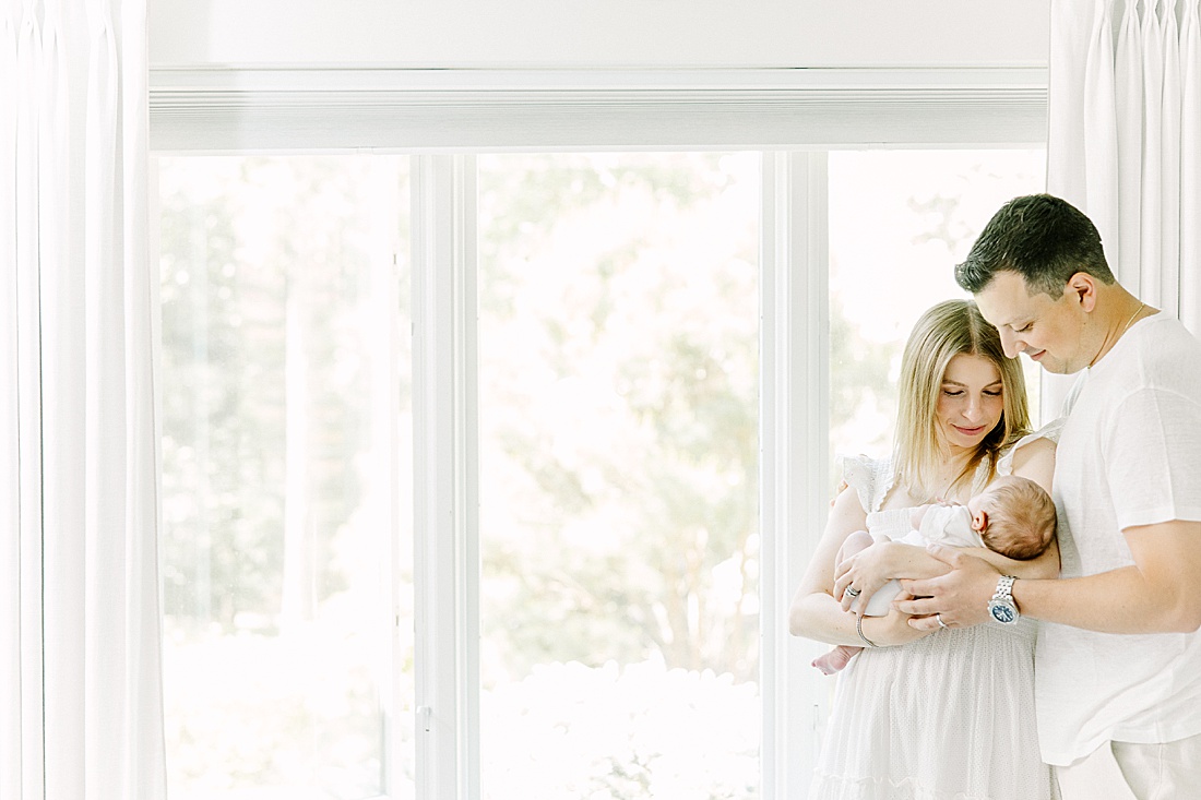 Parents hold baby near window during in-home newborn photo session with Sara Sniderman Photography in Natick Massachusetts
