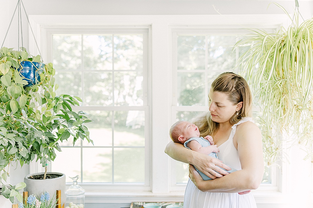 mother holds newborn by window during in-home newborn photo session with Sara Sniderman Photography in Metro West Boston. 
