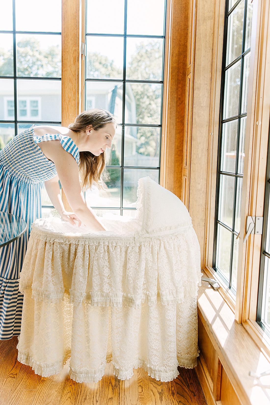 mother places baby into bassinet during in-home newborn photo session with Sara Sniderman Photography in Wellesley Massachusetts. 