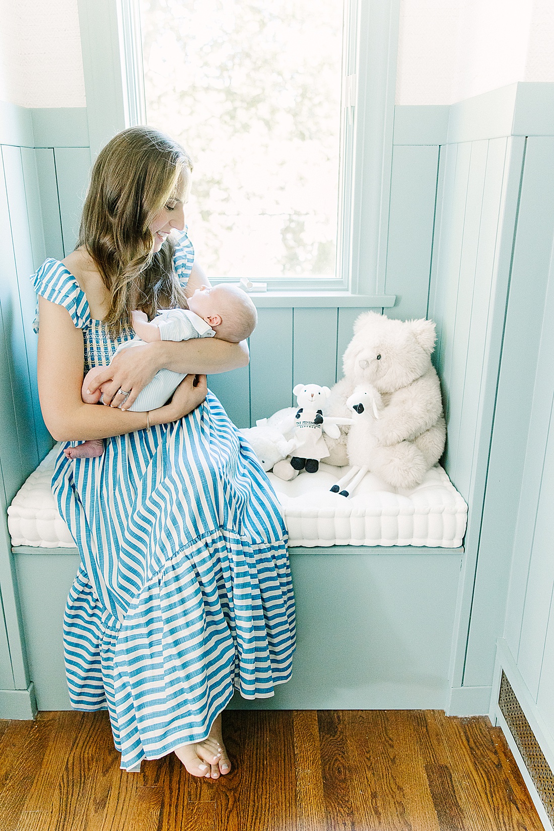 mother sits on window bench holding baby during in-home newborn photo session with Sara Sniderman Photography in Wellesley Massachusetts.